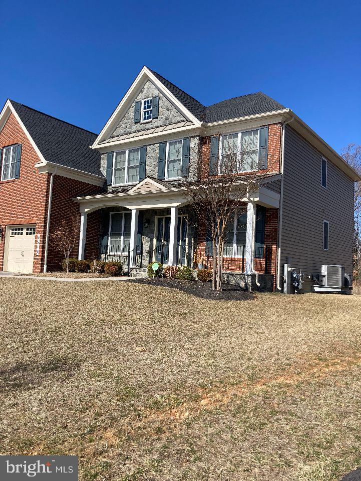 view of front facade with a garage, covered porch, cooling unit, and brick siding