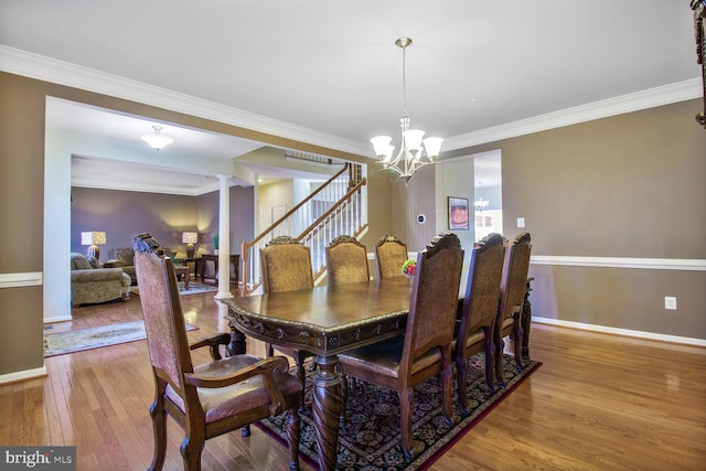 dining area with a chandelier, wood-type flooring, crown molding, and decorative columns