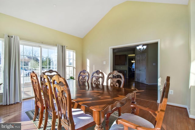 dining area featuring baseboards, high vaulted ceiling, wood finished floors, and an inviting chandelier