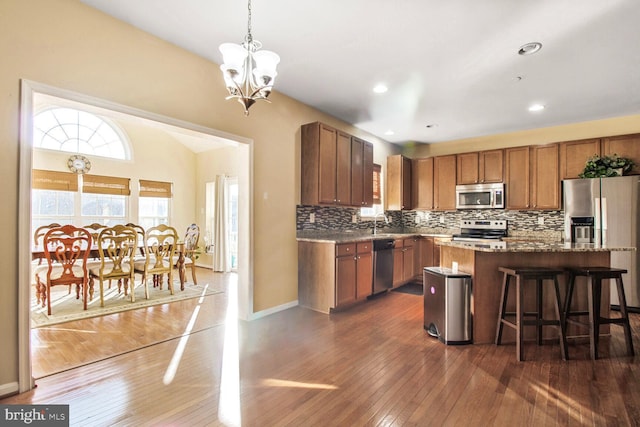 kitchen with a breakfast bar area, stainless steel appliances, tasteful backsplash, brown cabinetry, and dark wood finished floors