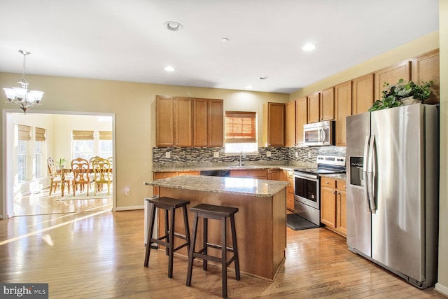 kitchen with appliances with stainless steel finishes, a sink, light wood-style floors, a chandelier, and backsplash