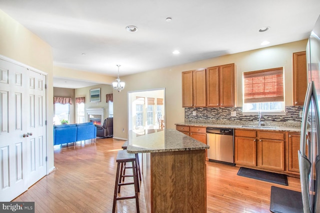 kitchen with decorative backsplash, appliances with stainless steel finishes, a sink, light stone countertops, and light wood-type flooring