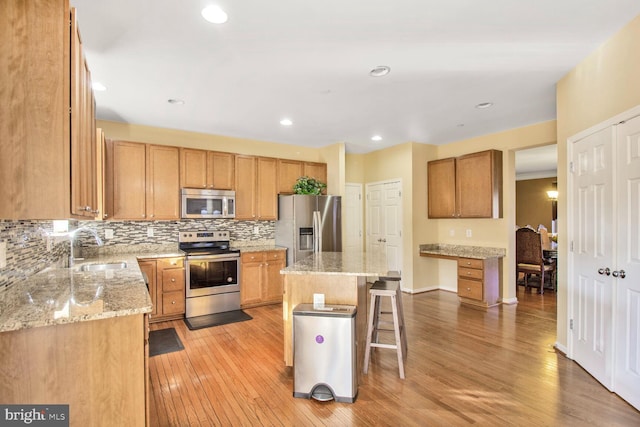 kitchen featuring light wood finished floors, a breakfast bar area, decorative backsplash, appliances with stainless steel finishes, and a sink