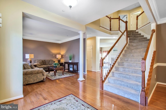 stairs featuring crown molding, decorative columns, baseboards, and wood finished floors