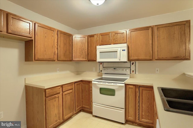 kitchen with brown cabinets, white appliances, light countertops, and a sink