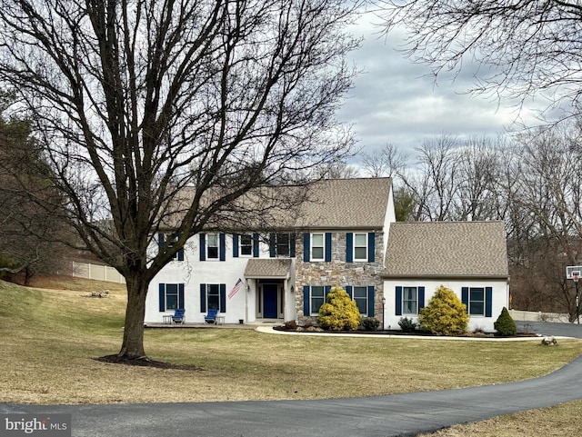 colonial house featuring stone siding and a front lawn