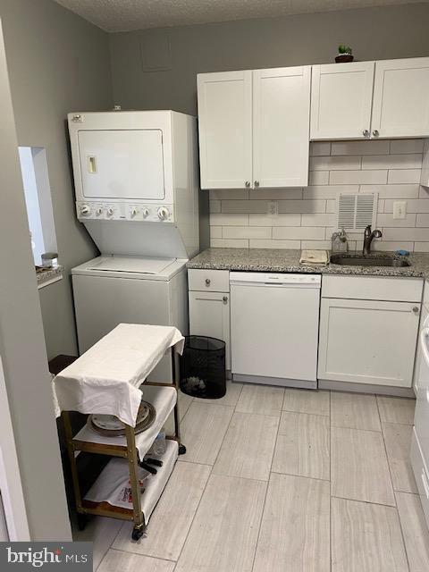 clothes washing area with laundry area, a sink, a textured ceiling, and stacked washing maching and dryer