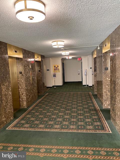 corridor featuring a textured ceiling, carpet floors, and elevator