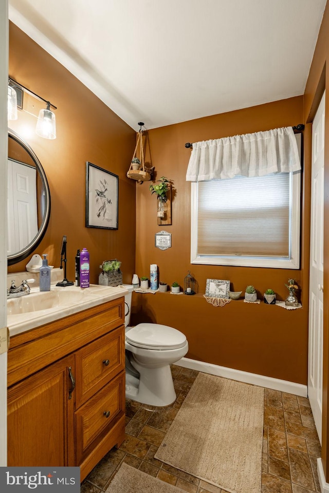 half bath with stone tile flooring, baseboards, vanity, and toilet