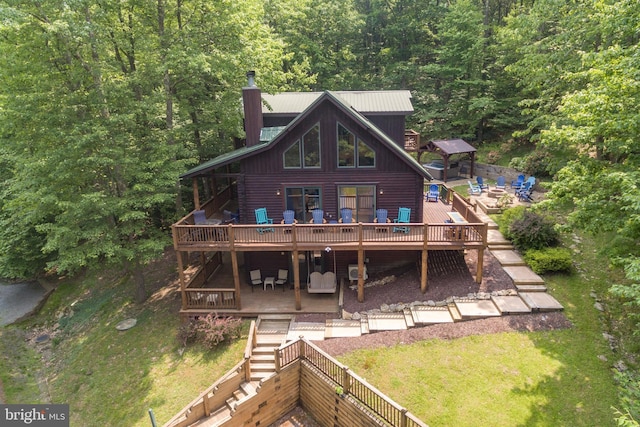 rear view of property with a chimney, a lawn, a deck, and a wooded view