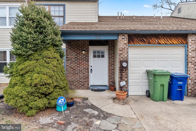 doorway to property featuring a garage, brick siding, and roof with shingles