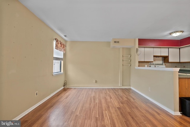 unfurnished living room featuring a sink, light wood-style flooring, visible vents, and baseboards