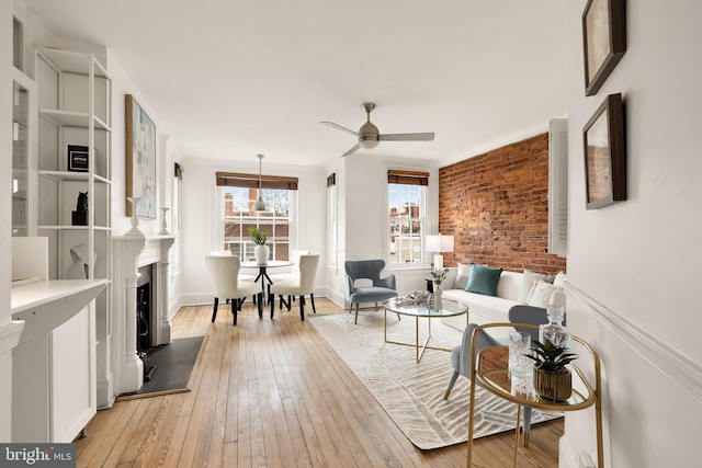 sitting room featuring brick wall, ornamental molding, light wood-type flooring, and a ceiling fan