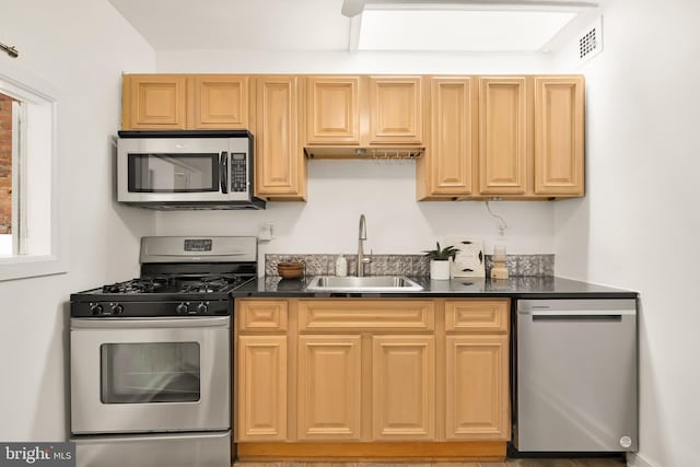 kitchen with stainless steel appliances, dark countertops, a sink, and visible vents