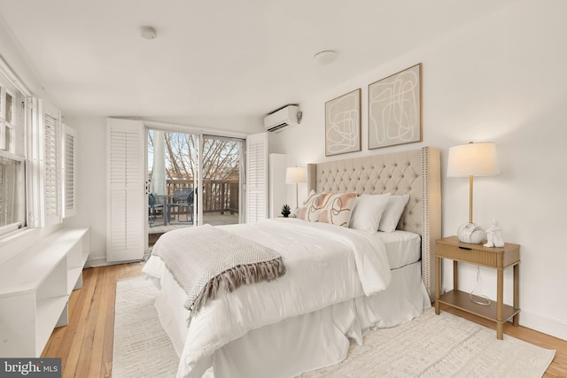 bedroom with a wall unit AC, access to exterior, light wood-type flooring, and baseboards