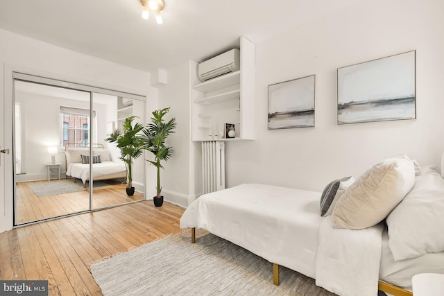 bedroom with a closet, radiator heating unit, a wall mounted AC, baseboards, and hardwood / wood-style flooring