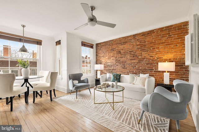 living room featuring light wood-style floors, crown molding, brick wall, and a ceiling fan