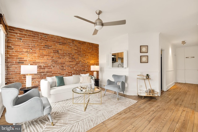 living room featuring baseboards, brick wall, a ceiling fan, and hardwood / wood-style floors