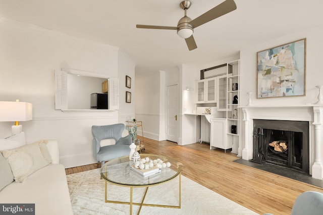 living room with ceiling fan, a fireplace, wood finished floors, and baseboards