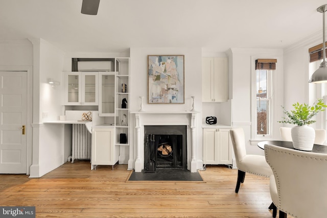 living area featuring radiator, light wood-style flooring, ceiling fan, and a fireplace with flush hearth