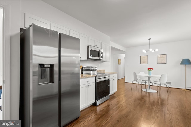 kitchen with dark wood finished floors, appliances with stainless steel finishes, light stone countertops, white cabinetry, and pendant lighting