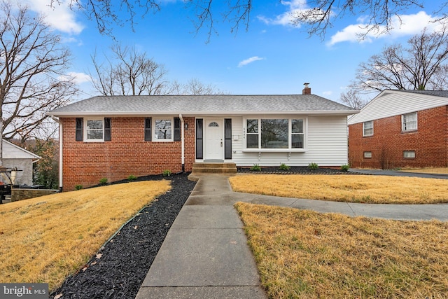 view of front of house featuring brick siding, a chimney, a front lawn, and roof with shingles