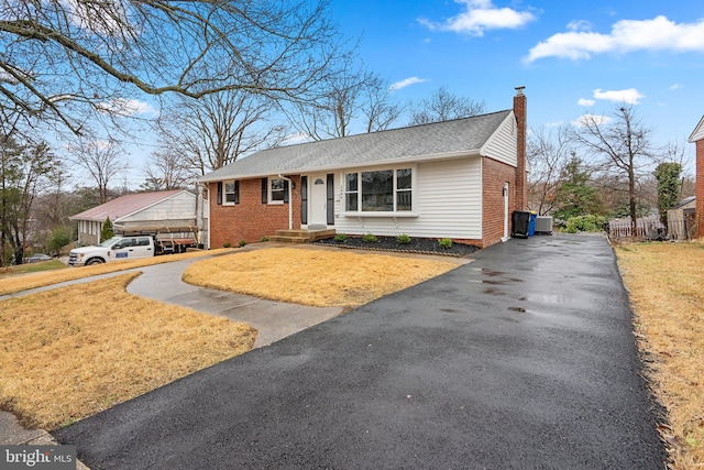 view of front of house featuring driveway, a chimney, a front lawn, and brick siding