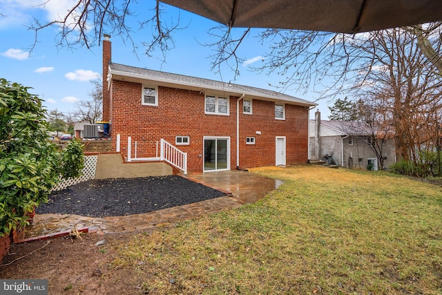 back of property featuring a chimney, brick siding, a lawn, and central AC unit