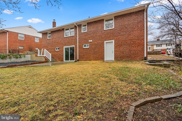 back of property featuring a chimney, a lawn, and brick siding