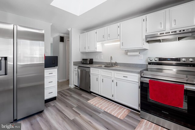 kitchen with under cabinet range hood, light wood-style flooring, stainless steel appliances, white cabinetry, and a sink