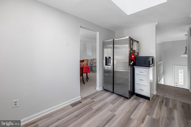 kitchen featuring baseboards, a skylight, light wood-style flooring, black microwave, and stainless steel fridge