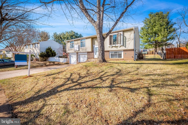 split foyer home with a front lawn, driveway, fence, a garage, and brick siding