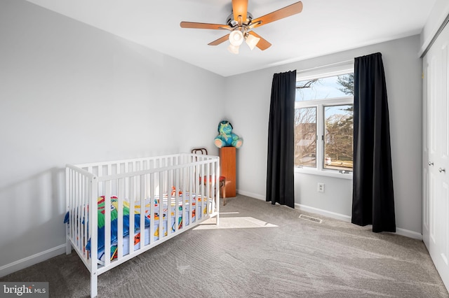 carpeted bedroom featuring visible vents, ceiling fan, a crib, and baseboards