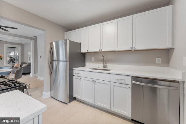 kitchen featuring appliances with stainless steel finishes, light wood-style floors, a ceiling fan, white cabinets, and a sink