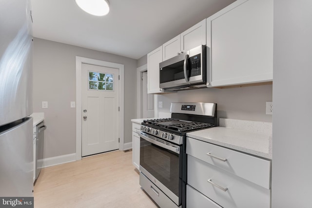 kitchen featuring light stone counters, stainless steel appliances, white cabinetry, baseboards, and light wood-style floors