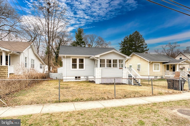 bungalow-style home with a fenced front yard, a sunroom, roof with shingles, and a front lawn