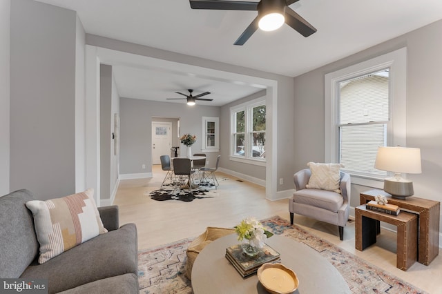 living room featuring baseboards, a ceiling fan, light wood-style flooring, and a healthy amount of sunlight