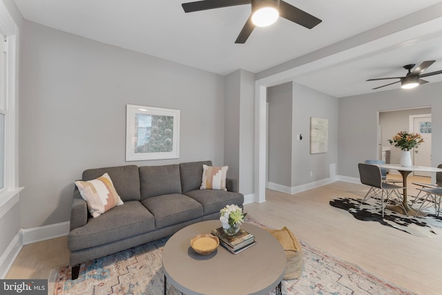 living area featuring light wood-style flooring, baseboards, and ceiling fan