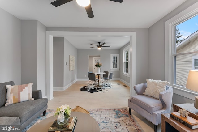 living area featuring light wood finished floors, plenty of natural light, baseboards, and a ceiling fan