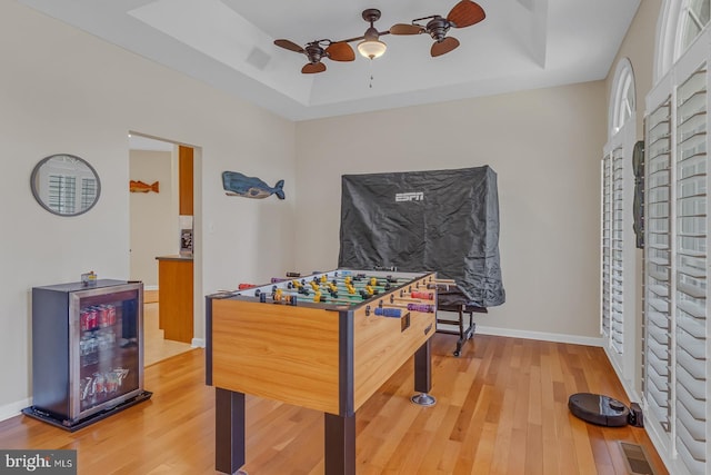 rec room featuring light wood-type flooring, a tray ceiling, and baseboards