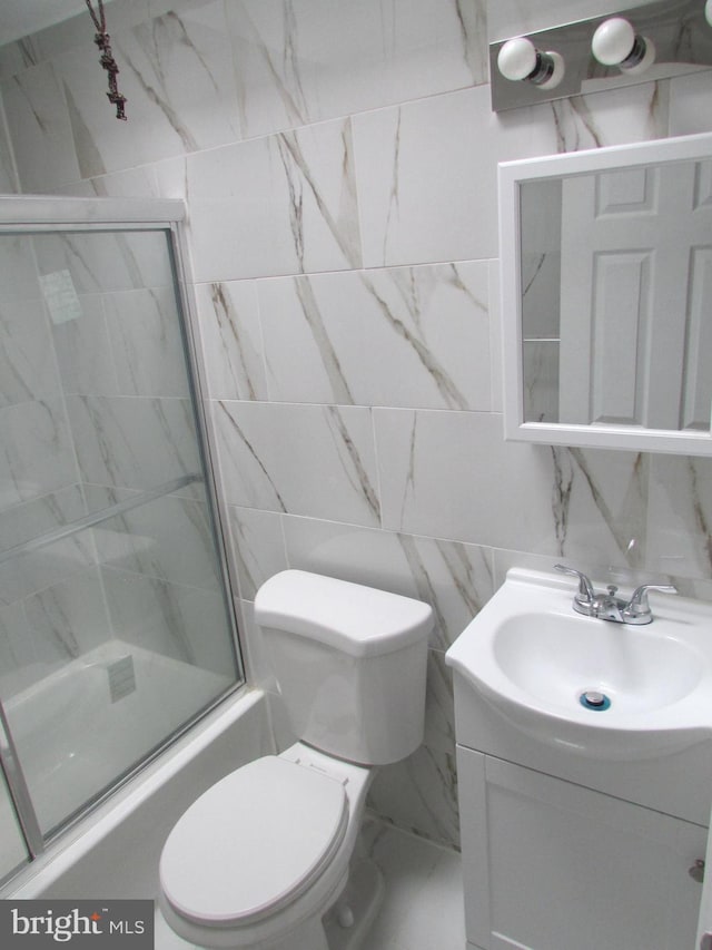 bathroom with toilet, marble finish floor, vanity, and tile walls