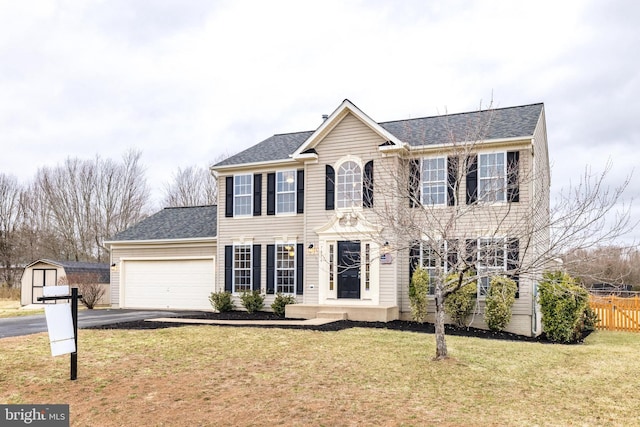 colonial home featuring a shingled roof, aphalt driveway, an attached garage, fence, and a front yard