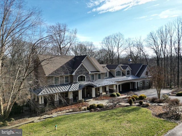 view of front facade with a front yard, driveway, a standing seam roof, covered porch, and metal roof