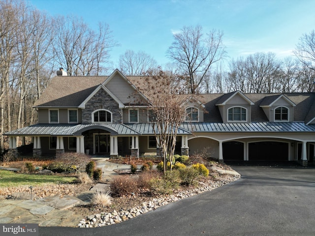 view of front facade featuring a porch, metal roof, stone siding, driveway, and a standing seam roof