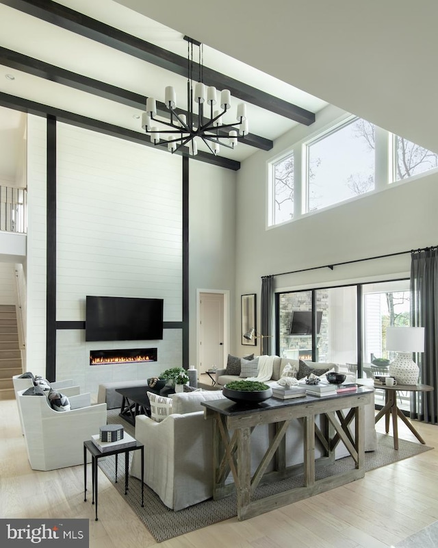 living area with beamed ceiling, an inviting chandelier, wood finished floors, and a fireplace