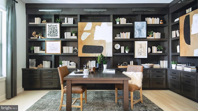 home office featuring baseboards, built in shelves, and wood finished floors