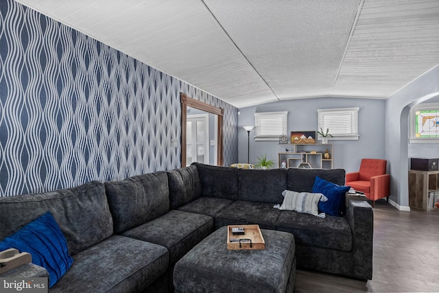 living room featuring wood finished floors, baseboards, wallpapered walls, vaulted ceiling, and an accent wall