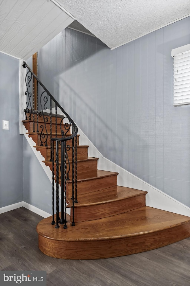 stairway with baseboards, a textured ceiling, and wood finished floors