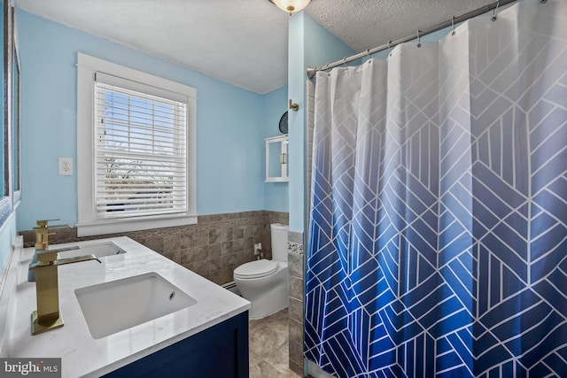 bathroom featuring double vanity, a textured ceiling, tile walls, and a sink