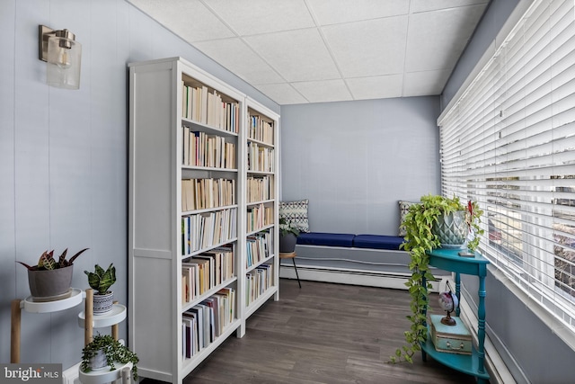 living area with a drop ceiling, a baseboard heating unit, and wood finished floors